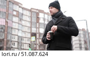 Handsome man wearing black coat and brown leather bag walking down on the city, drinking coffee paper takeaway cup with mobile phone. Stylish bearded middle-aged male using smartphone at urban street. Стоковое видео, видеограф Марина Демидюк / Фотобанк Лори