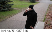 Handsome man wearing black coat and brown leather bag walking down on the city, drinking coffee paper takeaway cup with mobile phone. Stylish bearded middle-aged male using smartphone at urban street. Стоковое видео, видеограф Марина Демидюк / Фотобанк Лори