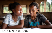 Two African students studying together in a rural classroom, with sunlight streaming in through the window. Black African children from disadvantaged families study in school, read books, receive primary education, volunteer service. Стоковое AI-изображение, AI-художник ALLA YURTAYEVA / Фотобанк Лори