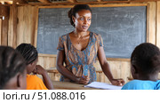An African teacher leading a discussion in a large classroom with enthusiastic students, modern educational technology. Black African children from disadvantaged families study in school, read books, receive primary education, volunteer service. Стоковое AI-изображение, AI-художник ALLA YURTAYEVA / Фотобанк Лори