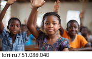 A group of African children raising their hands to answer questions in a lively and engaged classroom. Black African children from disadvantaged families study in school, read books, receive primary education, volunteer service. Стоковое AI-изображение, AI-художник ALLA YURTAYEVA / Фотобанк Лори