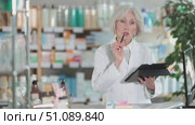 Mature female pharmacist works with a stylus on a tablet, she counts the leftovers of drugs in the pharmacy warehouse and plans a restock. Pharmacist works in a pharmacy. Стоковое видео, видеограф Яков Филимонов / Фотобанк Лори