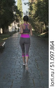 Rear view of young woman jogging along shady paved alley in park wearing grey sportswear with pink accents and sneakers on sunny morning with trees benches. Woman is engaged in sports and fitness. Стоковое видео, видеограф Сергей Тимофеев / Фотобанк Лори