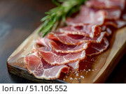 Thin slices of delicious speck alto adige pgi ham resting on wooden cutting board with rosemary. Стоковое AI-изображение, AI-художник Иван Рябоконь / Фотобанк Лори