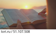 Woman reading Bible book on the beach at sunset with her fingers on the page. Стоковое видео, видеограф Ольга Сухарева / Фотобанк Лори