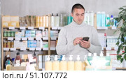 Young man with mobile phone choosing medicines and hygiene products in pharmacy. Стоковое видео, видеограф Яков Филимонов / Фотобанк Лори