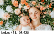 Heartwarming portrait of sleeping mother and her tiny baby, both wearing charming flower crowns and enveloped by vibrant, artistic arrangement of peach, white, and green blossoms, symbolizing love and. Стоковое AI-изображение, AI-художник Данила Большаков / Фотобанк Лори