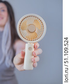 Young woman holding a mini cooling gadget feeling fresh and comfortable outdoors on a warm sunny day. Стоковое фото, фотограф Svetlana Golovco / Фотобанк Лори