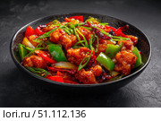 Sweet sour pork with colorful peppers, mixed vegetables served in a black bowl on dark concrete background. Traditional Chinese dish. Close-up. The meat pieces in a brown sauce glaze. Sichuan cuisine. Стоковое AI-изображение, AI-художник Марина Демидюк / Фотобанк Лори
