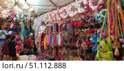 A colorful street market with lots of accessories and souvenirs. The stalls and stands feature colorful headbands, hair ties, headbands with flowers and decorations, toys, soft bags in the shape of cartoon characters, feathers and decorative elements. The atmosphere is that of a bustling Asian market, with many shoppers perusing the goods. The photo conveys the atmosphere of a fair or night market with an abundance of colors, textures and details. (2018 год). Редакционное фото, фотограф Анна Кривицкая / Фотобанк Лори