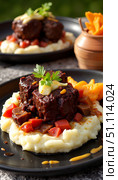 Braised short ribs served with mashed potatoes and vegetables on plate. Стоковое AI-изображение, AI-художник DeFusum / Фотобанк Лори