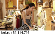 Young woman stands near denim clothes and chooses pants and shorts made of high-quality denim. European woman shopping in summer. Стоковое видео, видеограф Яков Филимонов / Фотобанк Лори