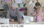 Mature dressmaker draws a sketch of a fashion design against the background of a assistant. Tailors work in the workshop. Process of creating clothes and drawing design on paper. Стоковое видео, видеограф Яков Филимонов / Фотобанк Лори