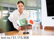 Positive young woman putting little flag of Pakistan on table next to the flag of Japan. Стоковое фото, фотограф Яков Филимонов / Фотобанк Лори