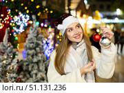 Girl in red Santa hat and with Christmas tree toys in her hands smiles dreamily. Стоковое фото, фотограф Яков Филимонов / Фотобанк Лори
