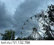 A Ferris wheel stands still against a backdrop of dark, stormy clouds and silhouetted trees. Concept of: Abandoned amusement. Стоковое фото, фотограф Ольга Петрова-Апостолова / Фотобанк Лори