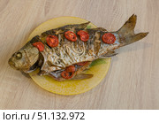 Baked large crucian fish with herbs, tomatoes and spices on a plate on the table. Стоковое фото, фотограф Екатерина Золина / Фотобанк Лори
