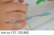 A close-up of the process of cross-stitch embroidery. A hand delicately guides the needle with blue thread through the white fabric. The complex art of embroidery. Стоковое видео, видеограф Воловодов Владимир / Фотобанк Лори