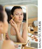 Woman applying eyeshadow with brush in front of vanity mirror. Стоковое фото, фотограф Яков Филимонов / Фотобанк Лори
