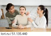 Sad woman sits silently in kitchen, adult girls sympathize and comfort her. Стоковое фото, фотограф Яков Филимонов / Фотобанк Лори
