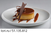 Spinning creme caramel glistening with golden caramel sauce, chocolate sprinkles highlighting smooth dessert surface on pristine white plate. Стоковое AI-видео, аниматор Юрий Поздников / Фотобанк Лори