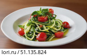 Zucchini noodles swirling with cherry tomatoes, basil, olive oil drizzling over white plate against weathered wooden backdrop. Стоковое AI-видео, аниматор Юрий Поздников / Фотобанк Лори