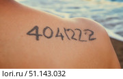 A person shows their tattoo of the number 404222 on their shoulder as waves crash in the background. Стоковое AI-видео, аниматор Данила Большаков / Фотобанк Лори