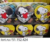 Display cases with gift sets of chocolate pralines in metal heart-shaped boxes with the image of the character Snoopy. The packages depict two design options: Snoopy with a red heart and Snoopy with a bouquet of flowers on a yellow background with polka dots. The colorful and cute packages create a festive atmosphere, perfect for Valentine's Day, birthdays or any romantic occasion. The bright tins serve not only as a container for the candies, but also as a souvenir that can be reused. The photo was taken in the store, several rows of products are presented on the shelves. (2019 год). Редакционное фото, фотограф Анна Кривицкая / Фотобанк Лори