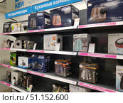 Shelves of a home appliance store with a variety of kitchen appliances. The display case features electric kettles, toasters, food processors, blenders and other kitchen appliances. Boxes with goods are located on metal shelves with price tags and information signs. Among the brands you can see Delonghi, Philips, Polaris, Vitek, Unit, Russell Hobbs, Braun. The top shelves are occupied by toasters, below are food processors, and a separate row is dedicated to electric kettles. The photo conveys the atmosphere of a modern electronics store and demonstrates the range of goods for cooking and household convenience. (2019 год). Редакционное фото, фотограф Анна Кривицкая / Фотобанк Лори