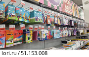 Shelves in a supermarket with a wide range of colored pencils and art supplies. The display case features sets from various brands: Krasin, Kruzhok and Dilin, Erich Krause, and other manufacturers. The pencils are packed in cardboard boxes with bright designs - images of animals, balloons, landscapes, cartoon characters, and geometric patterns. The range includes sets of 6, 12, 18, 24, and more colors. Prices are posted on individual price tags with promotional discounts. At the bottom of the shelf, stacks of sketchbooks and notebooks are visible. The photo is clear, with good detail, ideal for online stationery stores, catalogs of school supplies, educational materials, and advertising banners for stores specializing in children's creativity and preparation for school. Редакционное фото, фотограф Анна Кривицкая / Фотобанк Лори