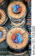 Seafood display cases in a supermarket. In the foreground are round plastic packages of White Leg shrimp, neatly arranged in a circle. In the center of each package is a serving sauce. On the lid is a bright blue label with the inscription Premium Club and information about the product. The shrimp are peeled, have a bright orange color and an appetizing appearance. The packages are stacked on top of each other in a metal refrigerated basket, with other seafood visible nearby. The photo is perfect for use in online stores, food catalogs, advertising materials for supermarkets and gastronomic services. Редакционное фото, фотограф Анна Кривицкая / Фотобанк Лори