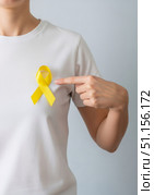 Сaucasian woman stands with a yellow ribbon on a white t-shirt, pointing at it. Стоковое AI-изображение, AI-художник Екатерина Селезнева / Фотобанк Лори