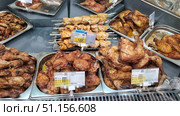 A counter with ready-made products in a supermarket, where a large amount of baked and fried chicken meat is presented. On the display case you can see trays with chicken legs, drumsticks, thighs and skewers with chicken kebabs. The meat has a golden crust and an appetizing appearance, seasoned with spices and is ready to eat. In the foreground are price tags indicating the cost per kilogram and the composition of the product. The image conveys the atmosphere of the grocery department of the supermarket and demonstrates the variety of chicken dishes for fast food and home dining. Редакционное фото, фотограф Анна Кривицкая / Фотобанк Лори