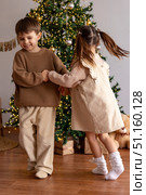 Happy little children, boy and girl holding hands, having fun and dancing near decorated Christmas tree in the morning. Merry Christmas and Happy New year winter holidays. High quality photo. Стоковое фото, фотограф Ирина Михайличенко / Фотобанк Лори