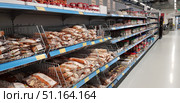 A long row of shelves in a modern supermarket. On the left, metal baskets hold bags of nuts and dried fruit in clear and brown packaging. On the right, jars and containers of spices, seeds, and other bulk products are placed. The shelves are neatly organized, the products are lined up in neat rows, and price tags are located under each section. The clean and spacious aisle emphasizes the order and modern atmosphere of the store.The image is great for illustrating themes related to retail, food, healthy living, choosing nuts, seeds, and spices, as well as for supermarket shopping concepts. (2019 год). Редакционное фото, фотограф Анна Кривицкая / Фотобанк Лори