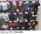 Shelves in an electronics store with a wide range of accessories for photo and video equipment. Various bags and cases for cameras and video cameras are hung on a perforated stand. The products vary in size, shape and color: there are compact hard cases, soft fabric bags, as well as options with handles and shoulder straps. There are models in black, gray, blue, red and combined colors. The display case has price tags and branded labels of manufacturers, among which there are Lowepro and other well-known brands. Cables and small accessories for photographic equipment are visible on the side section. The photo illustrates the store, retail equipment, assortment and choice of accessories for photographers and videographers. (2019 год). Редакционное фото, фотограф Анна Кривицкая / Фотобанк Лори