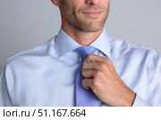 Businessman adjusting blue necktie, reflecting polished professional appearance and corporate confidence during morning preparation. Стоковое AI-изображение, AI-художник Юрий Поздников / Фотобанк Лори