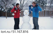 Young couple building snowman, carefully placing head and arms, laughing together during snowy backyard winter day. Стоковое AI-видео, аниматор Юрий Поздников / Фотобанк Лори