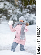 Little girl having fun playing with fresh snow during snowfall. Snowball fight. Kid dressed in warm clothes, hat, hand gloves and scarf. Active outdoors leisure for child on nature in snowy winter day. Стоковое фото, фотограф Ирина Михайличенко / Фотобанк Лори