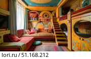 Art Deco-inspired kids room featuring vibrant curved furniture, stepped shelves, and metallic accents. Elegant space with child-friendly luxury and charm. Стоковое AI-изображение, AI-художник Светлана Леуто / Фотобанк Лори