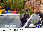 Женщина в форме полицейского из США беседует с мужчиной возле полицейской машины с включённой мигалкой на фоне разрушенного исторического здания. Редакционное фото, фотограф Владимир Шипикин / Фотобанк Лори