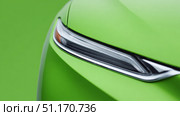 A close-up view of a modern green car’s sleek headlight design, showcasing its aerodynamic styling and glossy surface. The vibrant green color emphasizes eco-friendly aesthetics and futuristic automotive design. Стоковое AI-изображение, AI-художник Ксения Чунаева / Фотобанк Лори