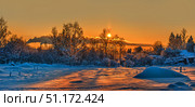 Winter landscape at sunset. In the foreground lies a snow field, illuminated by the bright orange-golden light of the setting sun. The snow plays with warm and cold shades, creating a glowing effect. On the horizon, trees covered with frost and snow are visible, through which the sun breaks through. In the sky, there is a soft gradient from orange to blue, with light clouds and traces of steam. The atmosphere of the photo is filled with tranquility, natural beauty and a sense of winter silence. Стоковое фото, фотограф Анна Кривицкая / Фотобанк Лори