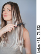 Young woman gently combing hair extensions with comfortable wide tooth comb for safe and easy styling. Стоковое фото, фотограф Svetlana Golovco / Фотобанк Лори