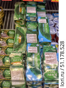 A supermarket refrigerated shelf with John West canned fish. In the foreground, green packages with the inscription John West are clearly visible - this is tuna in pieces in brine and other variations of canned fish. The packages are stacked in piles, creating a neat and dense row. Some of the cans are in triple packaging, which emphasizes the format of a bargain purchase. On the shelves on the left, you can see John West canned sprats in olive oil, and in the background - other fish products in round cans. The photo conveys the atmosphere of the store, which offers a wide range of seafood intended for everyday meals and gastronomic dishes. (2015 год). Редакционное фото, фотограф Анна Кривицкая / Фотобанк Лори
