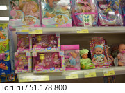In a children's goods store and shows shelves with dolls in boxes. In the foreground are baby dolls of different brands: Bigga, Simba and others. The toys are presented in bright packages with inscriptions and illustrations. Some sets include additional accessories: bottles, toys, clothes. In the top row, you can see dolls in the style of fairies and fairy-tale characters in colorful boxes. Price tags are placed on the shelves under each toy, the difference in cost is clearly visible. The atmosphere of the photo is bright and rich, it perfectly conveys the theme of childhood, toys and shopping in a supermarket. (2015 год). Редакционное фото, фотограф Анна Кривицкая / Фотобанк Лори