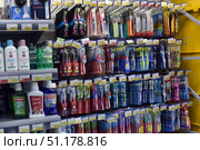 A department of the store with products for oral care. The shelves are filled with toothbrushes of various brands, such as Colgate, Oral-B, Parodontax and others. The range includes brushes with different bristle hardness, in packages of one or more pieces, as well as models with ergonomic handles and special attachments. Nearby are bottles of mouthwash, including Colgate Plax and Listerine. Price tags with promotional offers and discounts are visible above the products. The shelves are tightly organized, with bright packaging, which makes the display case visually rich. The atmosphere of the photo conveys the feeling of a wide selection of hygiene products in a modern supermarket. (2015 год). Редакционное фото, фотограф Анна Кривицкая / Фотобанк Лори