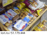 Supermarket counter with a variety of packaged pastries and cookies. In the frame you can see plastic containers with cookies of various shapes and types, as well as bright packages with waffles and pies. In the upper part of the photo you can see products in foil packages with inscriptions and images of finished products. In the lower part there is the inscription "Bread", indicating the department with bakery products. All products are neatly laid out in a wooden tray and are intended for retail sale. The atmosphere of the image conveys the usual assortment of confectionery products in the supermarket. (2015 год). Редакционное фото, фотограф Анна Кривицкая / Фотобанк Лори