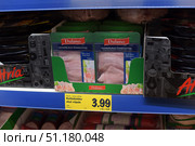 A shelf in a supermarket with sliced ​​ham of the Dulano brand. 400-gram packages with a green top and a transparent window through which thinly sliced ​​ham can be seen. Each package has a red brand logo and inscriptions in several languages. The product is displayed in a cardboard box with a green design and corporate symbols. A yellow price tag is attached under the shelf indicating the cost - 3.99 euros. Other meat products and sausages are visible on the left and right. The atmosphere of the frame is typical for a grocery store or supermarket demonstrating an assortment of meat delicacies. (2015 год). Редакционное фото, фотограф Анна Кривицкая / Фотобанк Лори