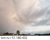Large beautiful cumulus clouds in evening sunset sky over rural area with houses and church , summer landscape. Стоковое фото, фотограф irisff / Фотобанк Лори
